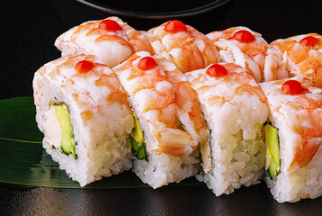 Sushi roll covered with shrimp meat on black ceramic plate
