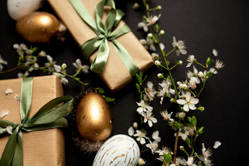 stylish dark easter layout with eco-wrapped gifts, golden and marble eggs, cherry blossoms on a black background. top view. copy space. flat lay. place for text