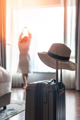 Traveller woman with luggage in business hotel guest room looking out toward city view staying for...