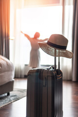 Traveller woman with luggage in business hotel guest room looking out toward city view staying for work travel or vacation trip - obrazy, fototapety, plakaty