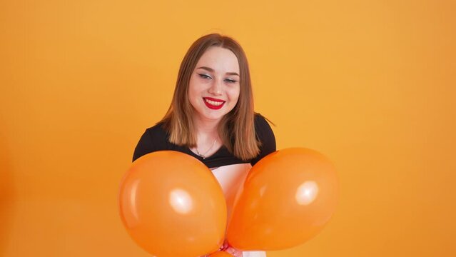 cheerful cheerleader with orange balloons posing on an orange background, medium shot. High quality 4k footage