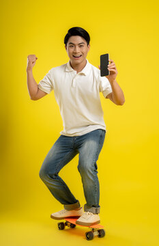 image of asian youth using mobile phone and playing skateboard on yellow background