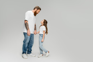 Side view of smiling dad and daughter holding hands on grey background.
