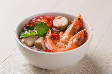 Tom Yum Goong served in white bowl on wood table. A Thai traditional spicy soup. Asian food.