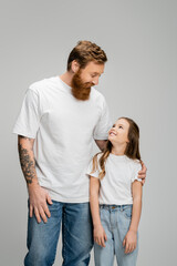 Fototapeta premium Tattooed father hugging preteen daughter isolated on grey.