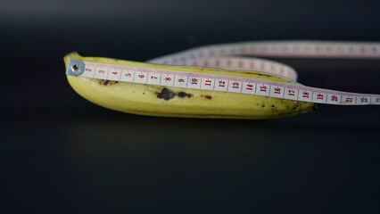 Yellow Banana with Measuring Tape Isolated on Black Background. comparable to man penis size as short, small medium, average, long,large size and extra large size