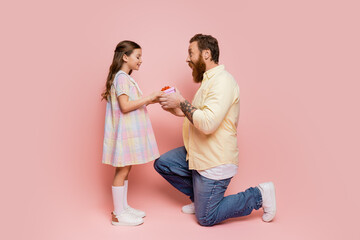 Side view of tattooed man giving gift to smiling daughter on pink background.