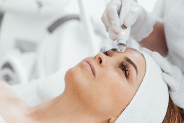 Obraz na płótnie Canvas Radiofrequency facial skin lifting. Hardware cosmetology RF lifting procedure and hardware facial massage. Rejuvenation, skin care in a beauty salon. Woman doctor cosmetologist and girl in spa clinic.