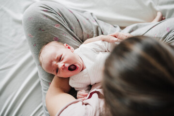 mother holding cute newborn baby girl yawning at home. Family concept