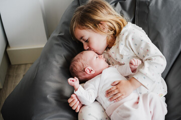 happy big sister toddler kissing newborn baby girl at home during daytime.Family and childhood