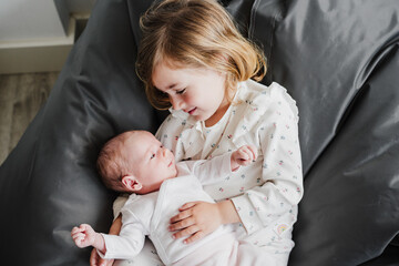 happy big sister toddler hugging newborn baby girl at home during daytime.Family and childhood