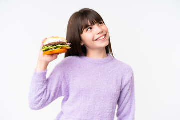 Little caucasian girl holding a burger over isolated background looking up while smiling