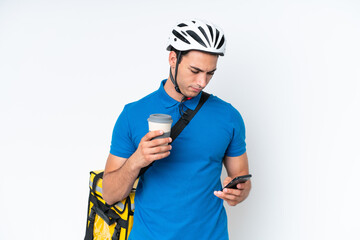 Young caucasian man with thermal backpack isolated on white background holding coffee to take away and a mobile