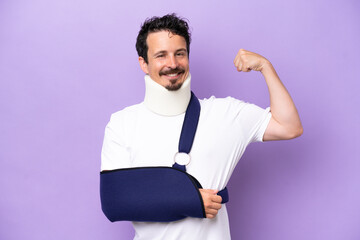 Young caucasian man wearing a sling and neck brace isolated on purple background doing strong gesture