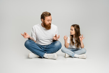 Kid and bearded dad doing gyan mudra while sitting on grey background.