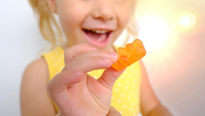 cheerful small child holds candy, blonde girl 3 years old wants eat gelatinous sweets with smile,...