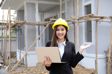 Attractive young construction worker smiling yellow hat working with laptop standing on building construction site. house building project