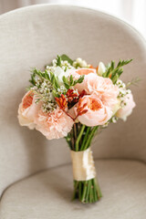 A fresh bouquet of pins and other flowers tied with a beige ribbon on the background of an armchair