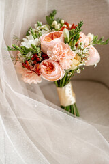 A bouquet of fresh pins and other flowers, tied with a beige ribbon, stands on a neatly laid out, delicate, cream-colored bridal veil with a splash of sequins.