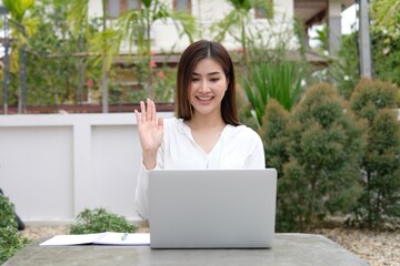 Laughing woman wearing pajama having video call on laptop during lunch break sitting at terrace in her home - summer time and video chat concept