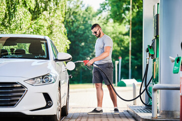 Confident man refueling his luxury auto. Driver with gasoline pump refilling car tank. Man in casual clothes and sunglasses refueling gas tank at modern gas station. - Powered by Adobe