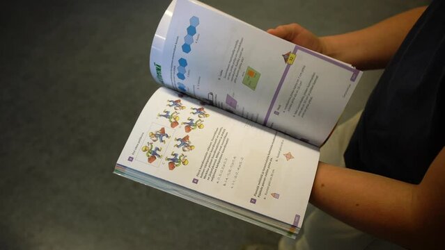 Boy turns pages of a maths textbook in a school corridor