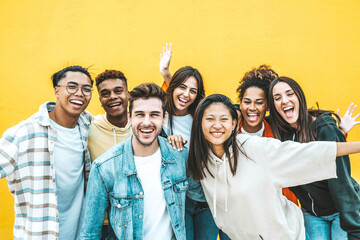 Multiracial group of young people standing in front of yellow isolated background - Youth community concept with guys and girls laughing looking at camera - Bright colors - obrazy, fototapety, plakaty