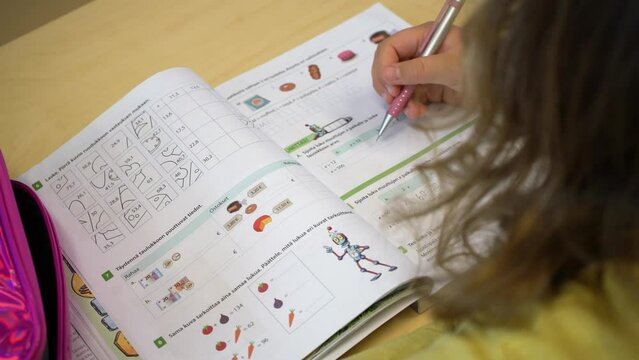 Girl with a pencil thinks over an elementary school maths textbook