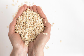 Hands full of oat flakes on white background. Super food rich in nutrients and that can be used for several recipes. Healthy eating. Top view and copy space.