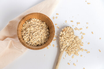 Wooden spoon full of oat flakes taken from a wooden bowl on a white background. Super food rich in nutrients and that can be used for several recipes. Healthy eating. Top view.