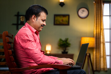Middle aged man busy working on laptop on chair at home - concept of technology, entrepreneur and surfing internet.
