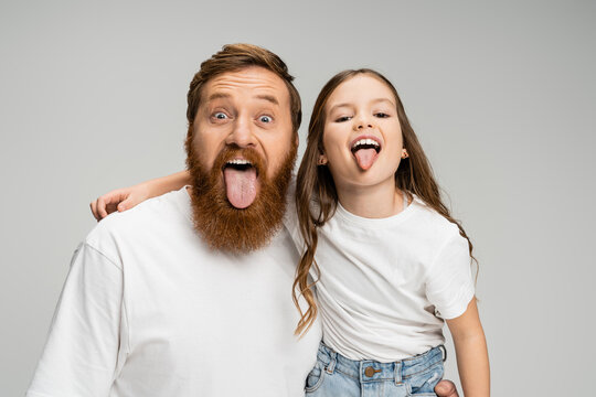 Preteen kid and bearded dad sticking out tongues isolated on grey.