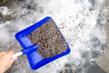 Fototapeta na wymiar Gravel used on slippery streets roads. Person scattering gravel sand on footpath to reduce slipperiness. Anti skid maintenance work. 