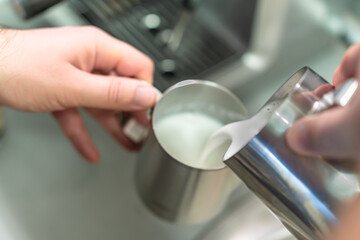 A man pours milk from one pitcher to another to make a cappuccino