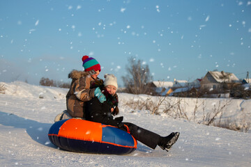 On a winter day, children go sledding and laugh merrily. A boy and a girl go down the mountain on a sled. Children in the winter in the village on vacation.