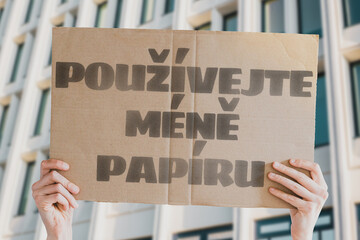 The phrase " Use less paper! " is on a banner in men's hands with blurred background. Human impact on the environment. Environmental degradation. Nature. Forest. Trees. Modern technology