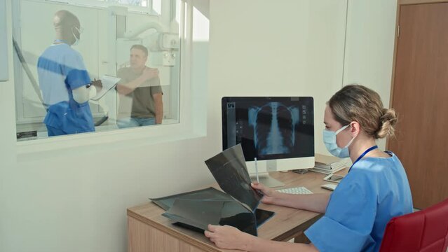 Female radiologist sitting at desk working with X-ray images while her colleague consulting patient
