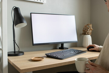 Person working  from home on laptop with larger monitor in the background and holding a coffee mug.
