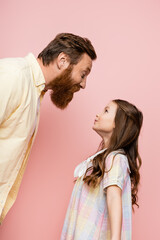 Side view of cheerful dad and preteen daughter standing isolated on pink.