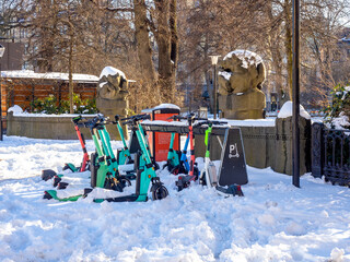 Rent of electric scooters in the snow on the street of Stockholm against the backdrop of the city park