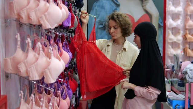 Two girls in a romantic relationship together choose underwear, bras and lingerie together in a women's lingerie store in a mall. Women consult before making a purchase, girlfriends shopping together
