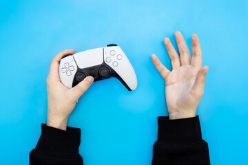 A male hands hold a gamepad on a blue background. Concept of the game, e-sports, leisure, gaming industry, video games, top view. © sav_an_dreas