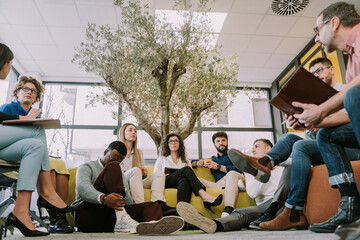 A young black male person checking his phone while his coworkers are having a business talk