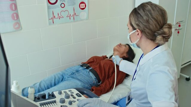 Female medical specialist wearing protective mask and gloves doing medical ultrasound scan for young patient