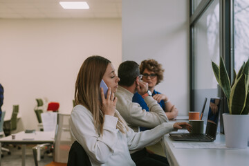 Stunning blonde businesswoman having phone call while working on her lap top. her middle-aged colleagues are having a conversation in the back