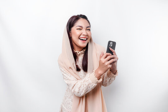 A Portrait Of A Happy Asian Muslim Woman Wearing A Headscarf, Holding Her Phone, Isolated By White Background