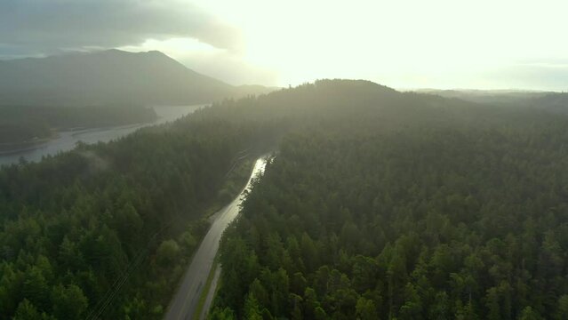 White Car driving Lush green forest road Ucluelet Vancouver Island British Columbia Misty island mountains West Coast Canada Pacific Ocean coast. Golden sunrise blue water aerial