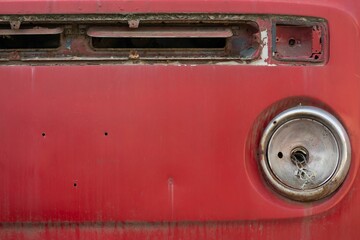 Closeup shot of the front part of an old vintage rusty red car on the blurred background
