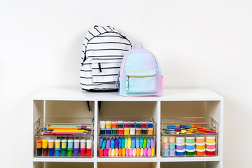 White shelving with kids backpack and various material for creativity and art activity. Stationery...