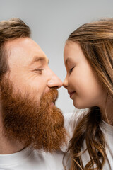 Side view of bearded dad and preteen daughter standing nose to nose isolated on grey.